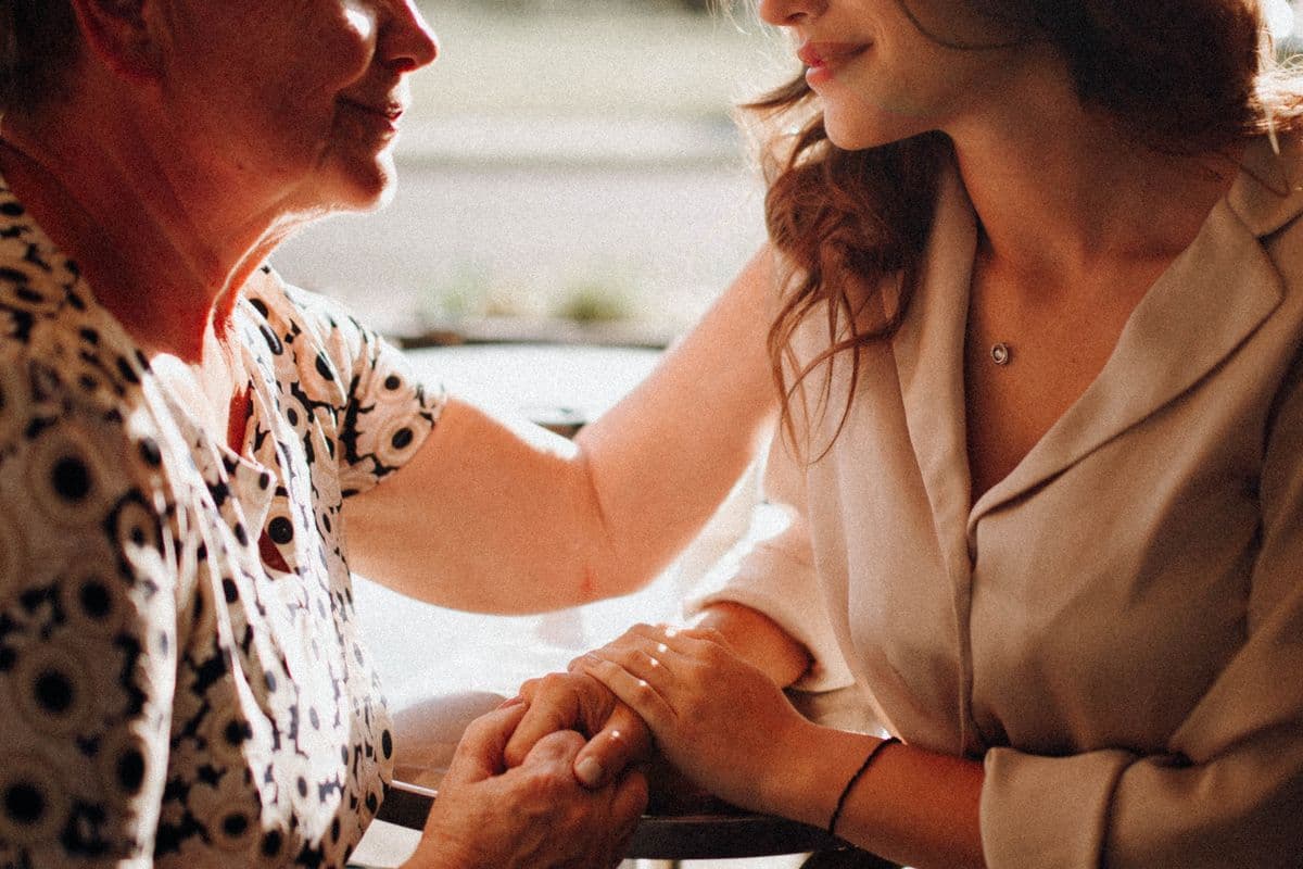 An older woman and her adult daughter sitting close and holding hands.