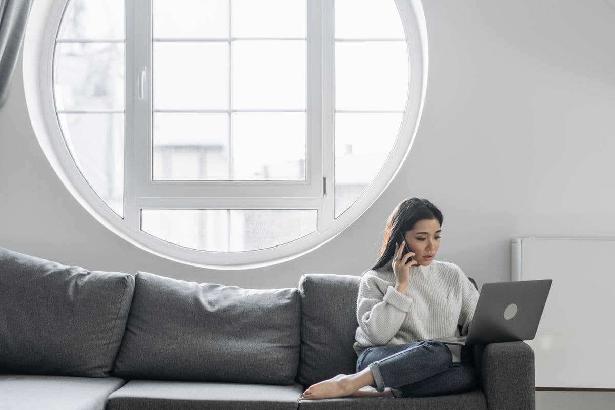 A woman at home on the phone with a laptop, coordinating care from a distance.